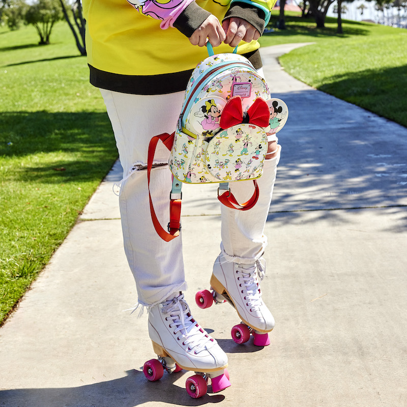 Image of woman outside wearing roller skates and holding the Loungefly Disney100 Mickey & Friends Classic All-Over Print Iridescent Mini Backpack with Ear Headband 